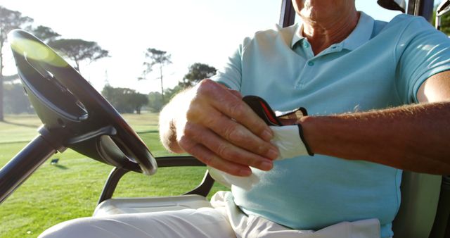 Golfer sitting in golf buggy wearing golf glove at golf course