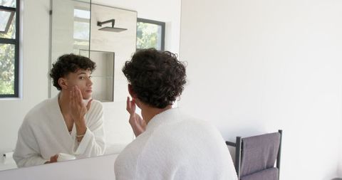 Man Perfecting Skincare Routine with Natural Light in Modern Bathroom