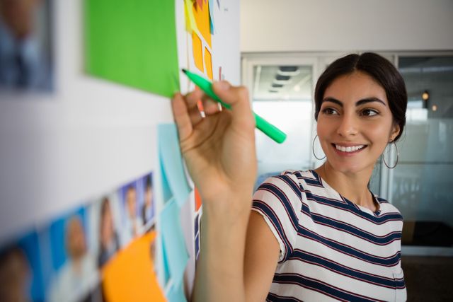 Smiling young woman writing on sticky note in creative office