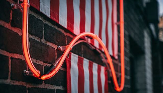 Neon tube glowing over brick wall with red-white striped banners