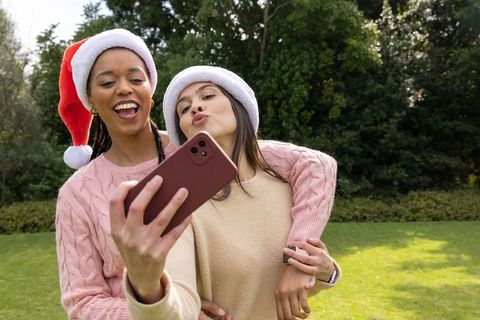 Friends taking festive holiday selfie outdoors wearing santa hats and cozy sweaters