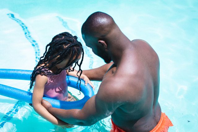 African american father helping daughter with swimming float in pool on sunny day. unaltered, enjoyment, family, lifestyle and togetherness.