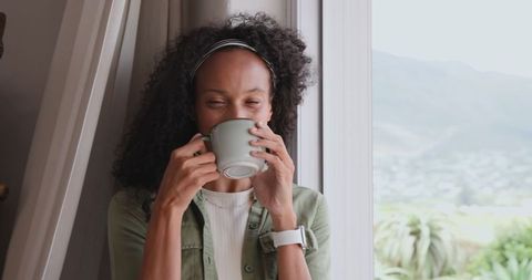 African american woman relaxing with tea by window at home