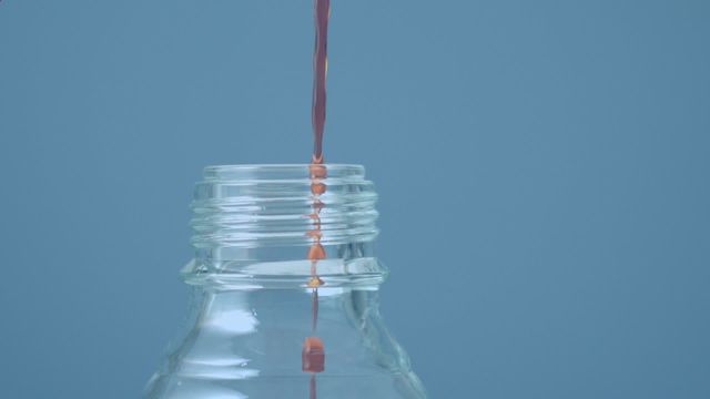 Liquid pouring into glass bottle with animated red shapes on blue background suggests concept of science experiments or chemistry. Useful for educational content, lab demonstrations, illustrative purposes in scientific discussions, or digital animation showcases.