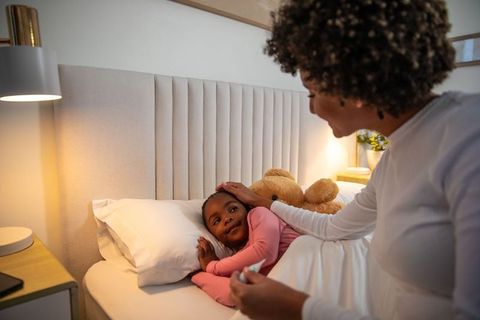 Mother comforting daughter with digital thermometer and teddy bear