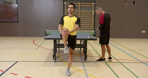 Teammates Stretching in Gym with Table Tennis Setup