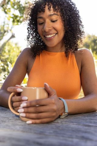 Smiling Woman Relaxing Outdoors with Coffee Mug and Fitness Tracker