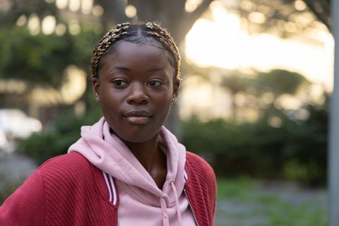 African american woman wearing pink hoodie and red jacket standing in park at golden hour