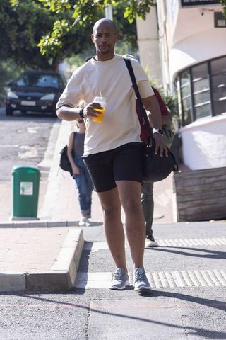 African american man walking with duffel bag and cold orange drink on sunny urban sidewalk