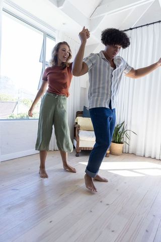 Young couple dancing barefoot in bright airy living room holding hands on light wood floor