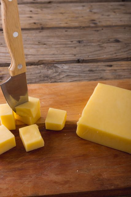 Close-up of knife on cheese cubes on wooden board at table, copy space. unaltered, food and dairy product.
