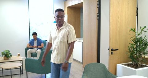 Contemporary coworker lounge with black man walking and asian coworker checking smartphone