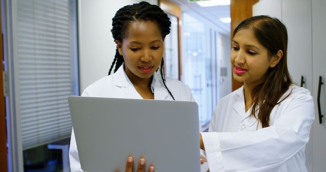 Two healthcare professionals, an African American and an Asian, are engaged in a discussion over a laptop, with copy space. Their collaboration highlights the importance of teamwork in medical settings.