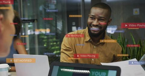 Smiling team leader guiding discussion with laptops and ui overlays in glass workspace