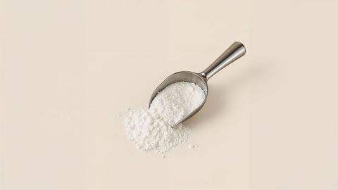 Stainless steel scoop with white milk powder on beige surface