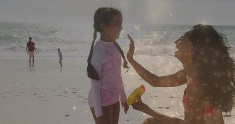 Mother applying sunscreen on daughter's face at sunlit beach