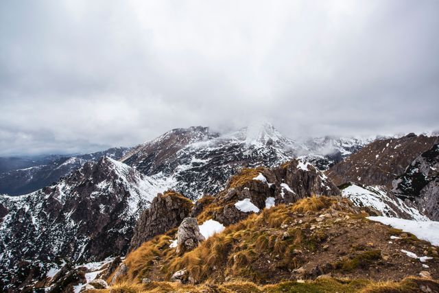 Mountain peaks covered in mist with snow-covered cliffs perfect for showcasing rugged landscapes. Ideal for adventure blog posts, travel promotions, or nature-themed prints.