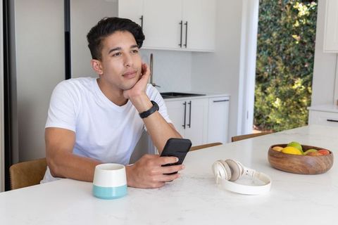 Contemplative african american man sitting at modern marble kitchen island holding smartphone