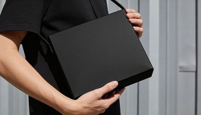 Matte black shoulder bag held by male in black tee with urban minimalist background