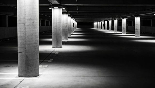 Receding concrete columns casting light pools and shadows in monochrome parking garage