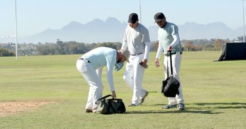 Diverse male teammates preparing gear on grassy sports field with goal posts and mountains