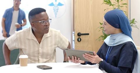 Patient consulting with female healthcare worker wearing hijab using tablet in clinic