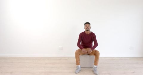 Pensive young man sitting indoors in casual outfit