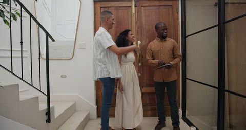 Diverse couple welcoming friend at modern home entrance