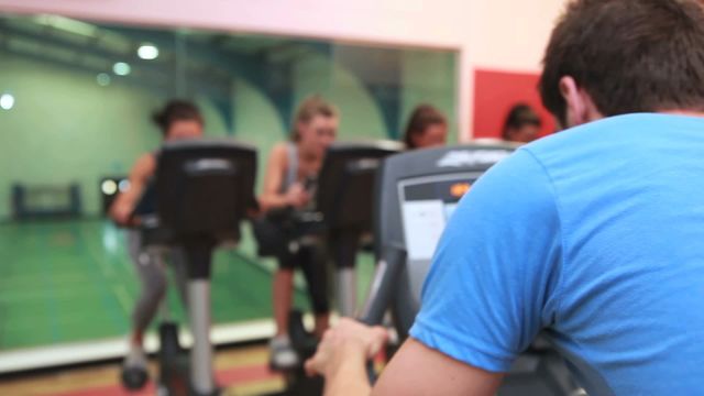 Fitness trainer leading a group of people on stationary bikes at a gym. Useful image for promoting health, fitness, group training, and active lifestyles. Ideal for advertising fitness programs, gym memberships, or educational materials about physical fitness.