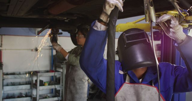 Image of two diverse female car mechanics welding car. working in car repair shop and running small feminine business concept.