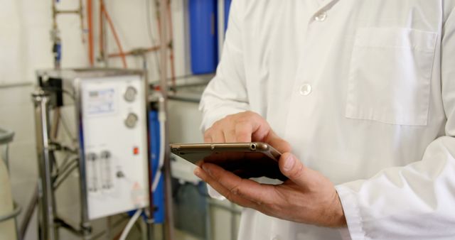 Professional in a lab coat using a smartphone in an industrial setting. They are monitoring processes or communicating with colleagues.