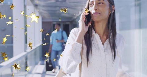 Professional woman walking skybridge talking on smartphone with rolling suitcase and stars