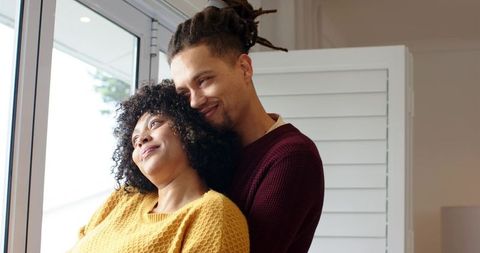 Cozy morning embrace by window, couple cuddling in knit sweaters with soft daylight