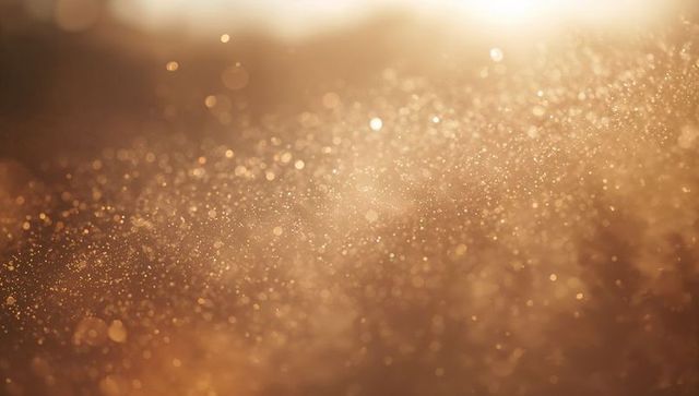 Floating golden dust particles catching sunlight with warm bokeh glow and amber sparkle