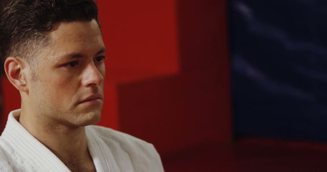 Martial artist appears deep in thought in this candid moment, wearing a traditional white gi. Ideal for articles or promotions related to martial arts training, personal discipline, mental focus, and physical conditioning.