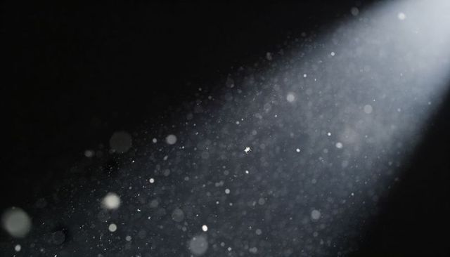 Spotlit snowflake floating in dark studio with dust particles and bokeh glow
