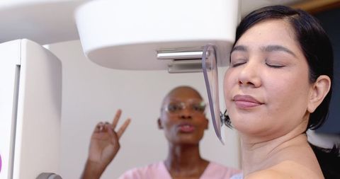 Asian woman undergoing mammogram while black technologist giving reassurance gesture