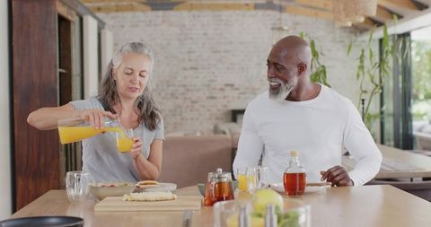 Mature interracial couple enjoying breakfast with orange juice in bright open kitchen
