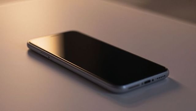 Modern smartphone lying diagonally on matte desk with warm reflective light and moody glow