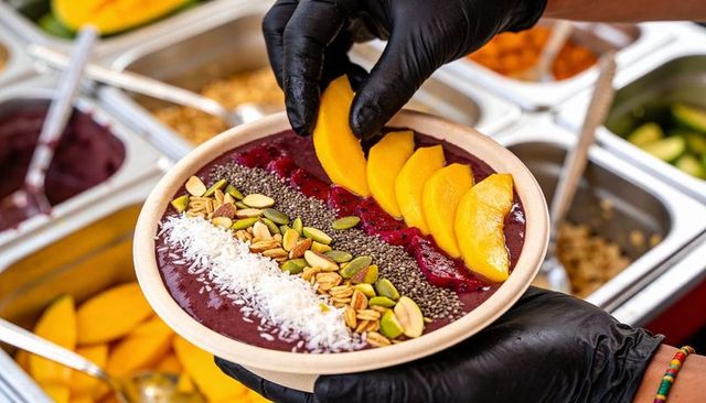 Placing mango slices on acai bowl with chia seeds coconut granola at juice bar counter