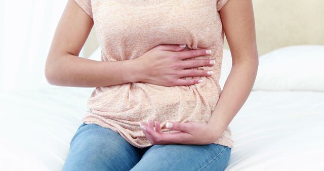 Woman Holding Stomach in Pain While Sitting on a Bed - Download Free Stock Images Pikwizard.com