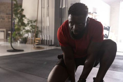African american man tying shoe kneeling on rubber floor before intense workout