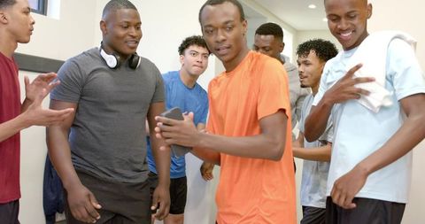 Diverse male teammates gathering around player sharing smartphone in locker room