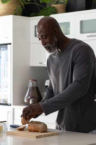 Senior african american man calmly slicing artisan bread at modern sunlit kitchen island
