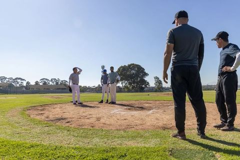 Baseball coaches guiding players on mound in sunny practice discussing pitching strategy