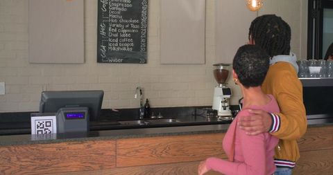 Couple checking chalkboard menu at coffeehouse counter in mustard jacket and pink sweater
