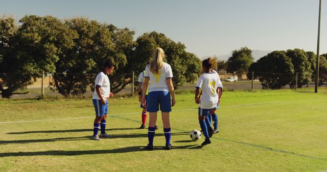 Group of female soccer players practicing on soccer field under clear sky. Ideal for use in sports marketing, athlete health campaigns, youth activity advertisements, and empowerment promotions.