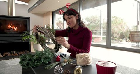 Woman crafting holiday wreath by fireplace in cozy living room
