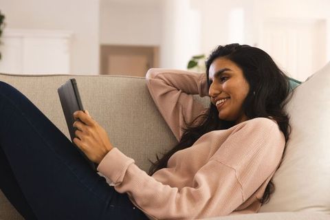 Woman Relaxing on Couch Using Tablet and Smiling