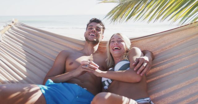 Couple enjoying sunny day, lying in hammock, and smiling under palm tree. Ideal for promoting travel, tourism, and beach resorts. Suitable for advertisements showcasing vacation destinations, outdoor relaxation, and relationship bonding activities.